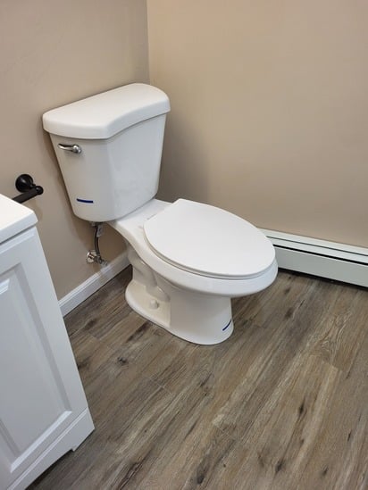 Detail of a new efficient toilet and baseboard heating unit placed on water-resistant flooring during the bathroom remodel Shrewsbury.