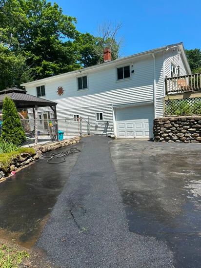 Landscape perspective showcasing a wide section of the asphalt driveway sealcoating leading toward a white residential building and fenced pool area.